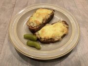 Two open-faced tuna melt sandwiches on a plate with two baby pickles