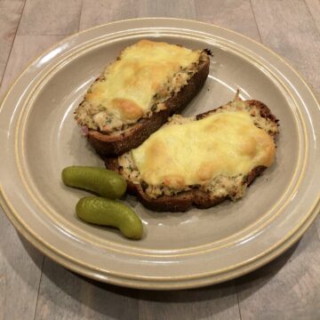 Two open-faced tuna melt sandwiches on a plate with two baby pickles