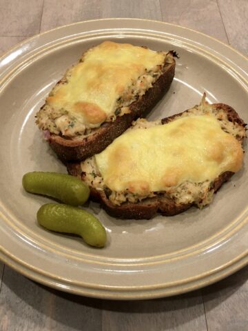 Two open-faced tuna melt sandwiches on a plate with two baby pickles