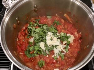 Large pot over stove with tomato soup and new basil and Parmesan addition